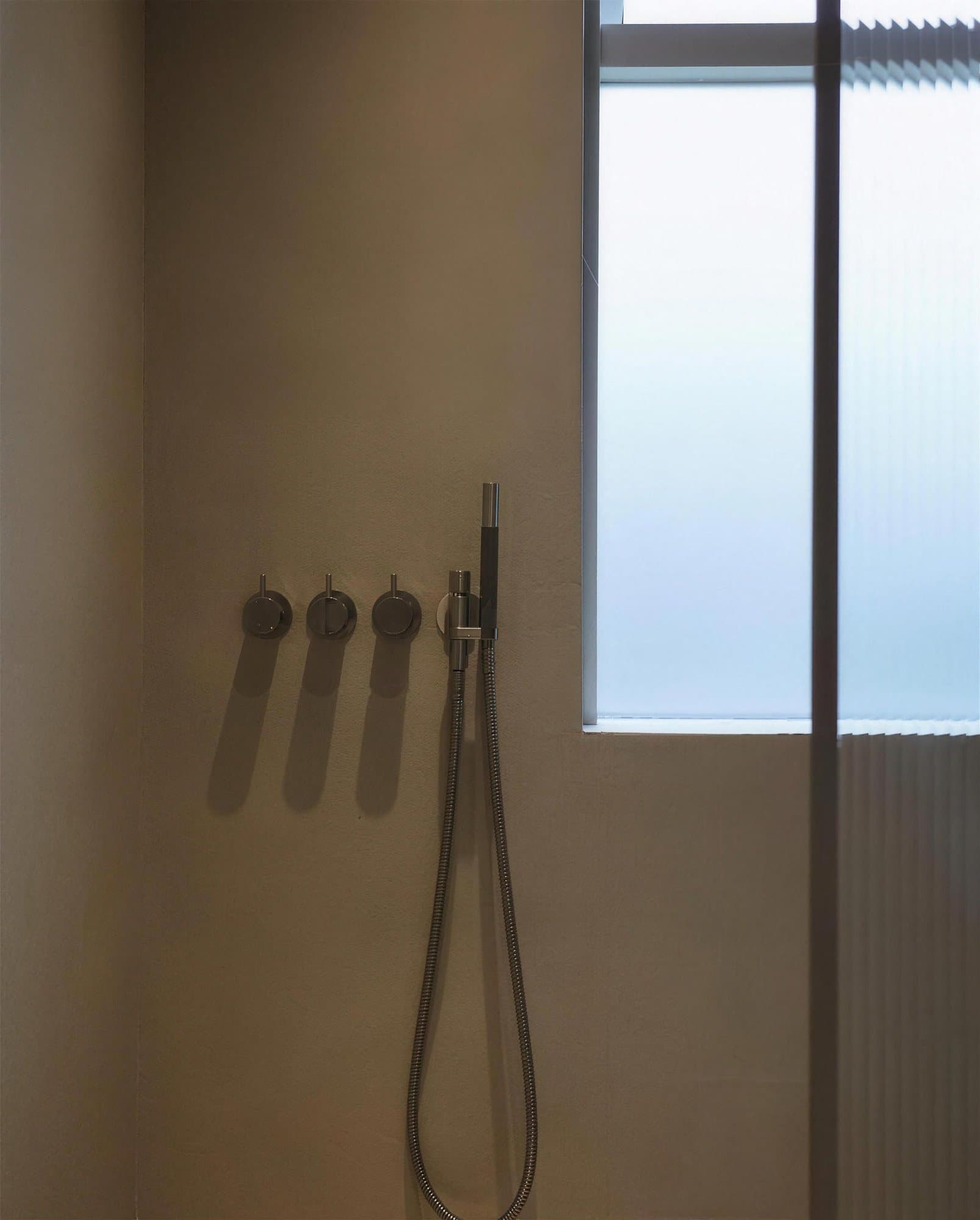 Sturta með microcement á veggjum, blöndunartæki úr stáli og gluggi